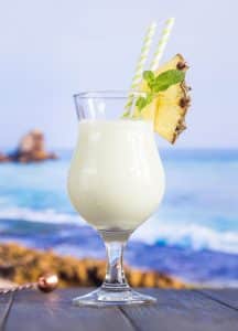 Cocktail Pina Colada în pahar hurricane, garnisit cu felie de ananas