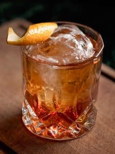 Cocktail Old Fashioned cu bourbon, cub de gheață și coajă de portocală