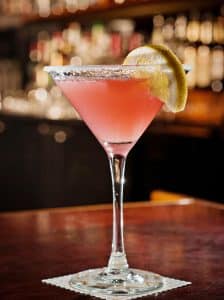 Cocktail Cosmopolitan roz, servit în pahar de martini cu felie de lime