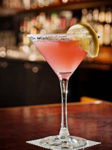 Cocktail Cosmopolitan roz, servit în pahar de martini cu coajă de lime