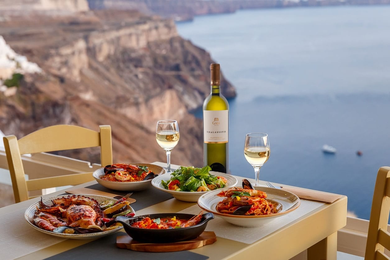 Pahar și sticlă de vin alb pe o terasă din Santorini, cu vedere la Marea Egee